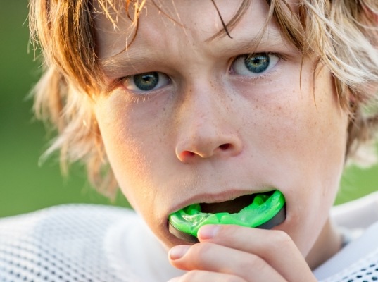 Young boy putting green athletic mouthguard over his teeth