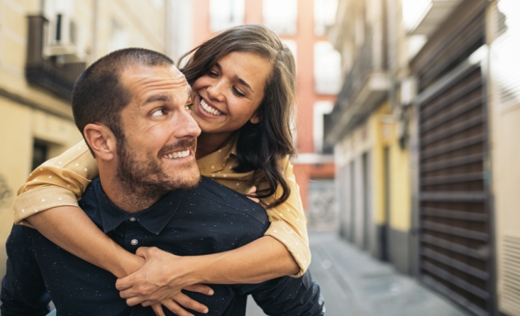 Smiling woman and man holding each other outdoors after restorative dentistry in Longmeadow