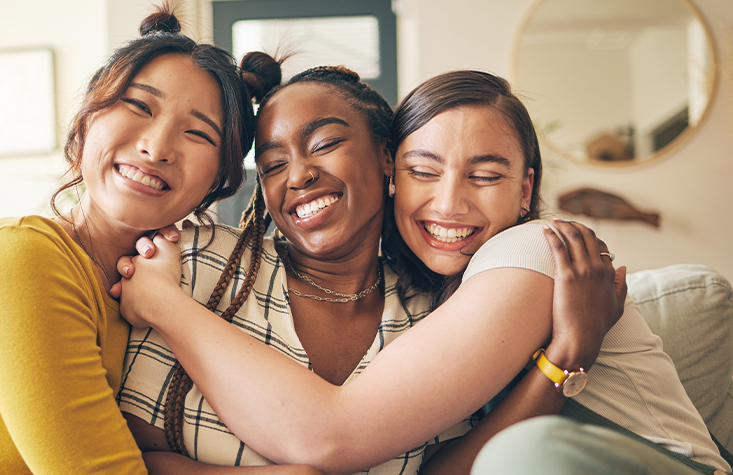 Three women hugging and smiling on couch together