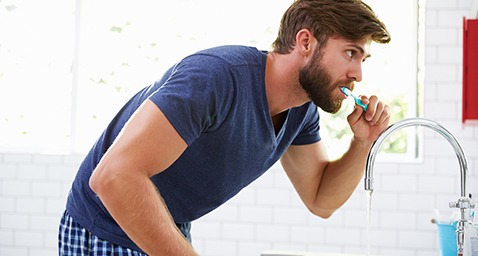 Man in blue shirt brushing his teeth in bathroom